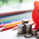 Close up picture of a red piggy bank, some colored pencils and some glasses on top of a desk