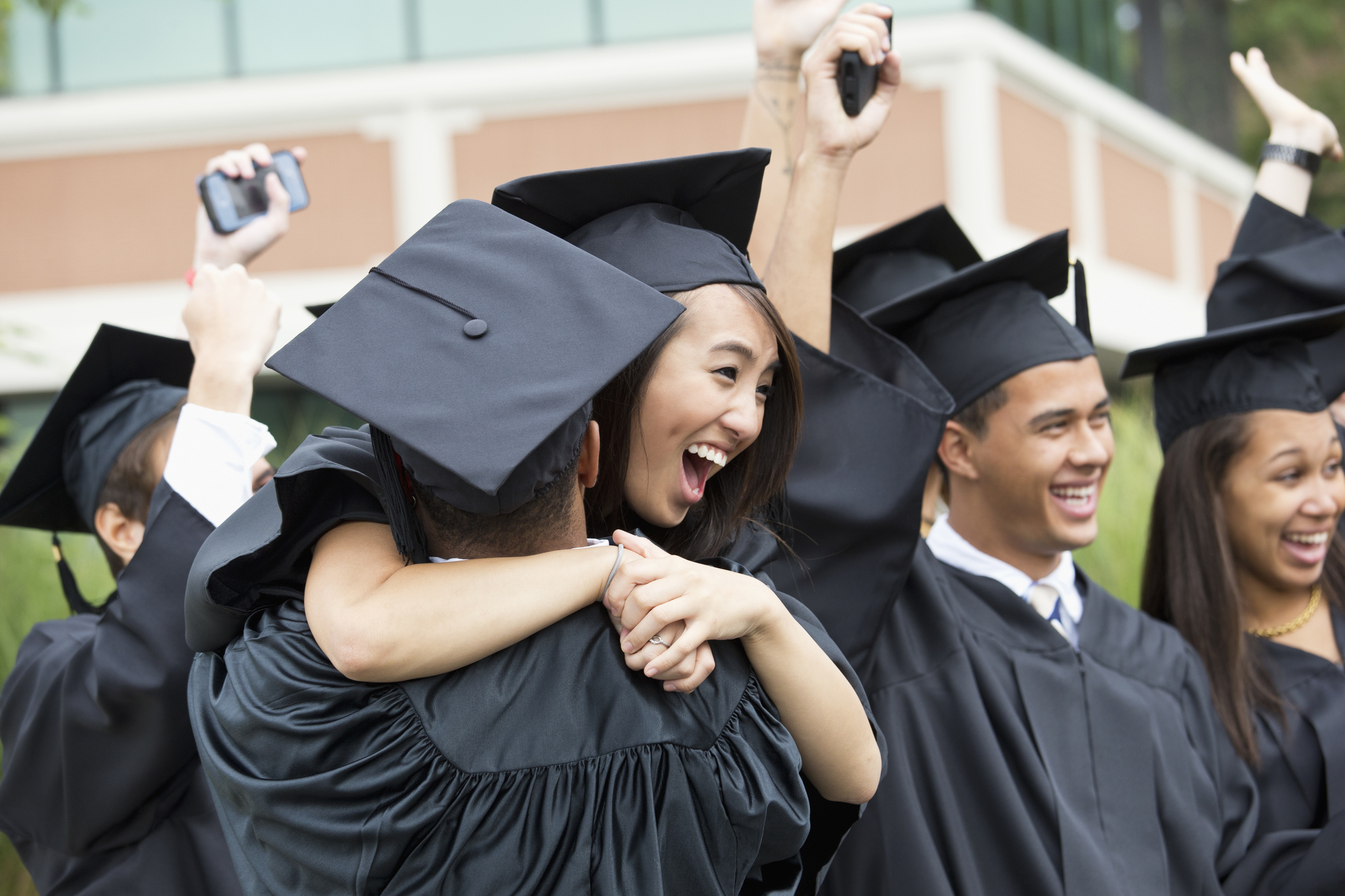 A group of college students dressed in caps and gowns congratulate and hug each other on graduation day.