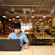 A male Asian American college student sitting at a table in a student center. He has his laptop open, and is using his credit card to pay for a school tuition bill online.