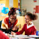 A Black female elementary school teacher helps a student in her classroom with homework.