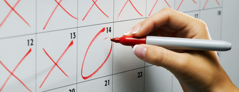 Close up of a college graduate using a red sharpie pen to mark off days on a calendar until she pays off her student loans.