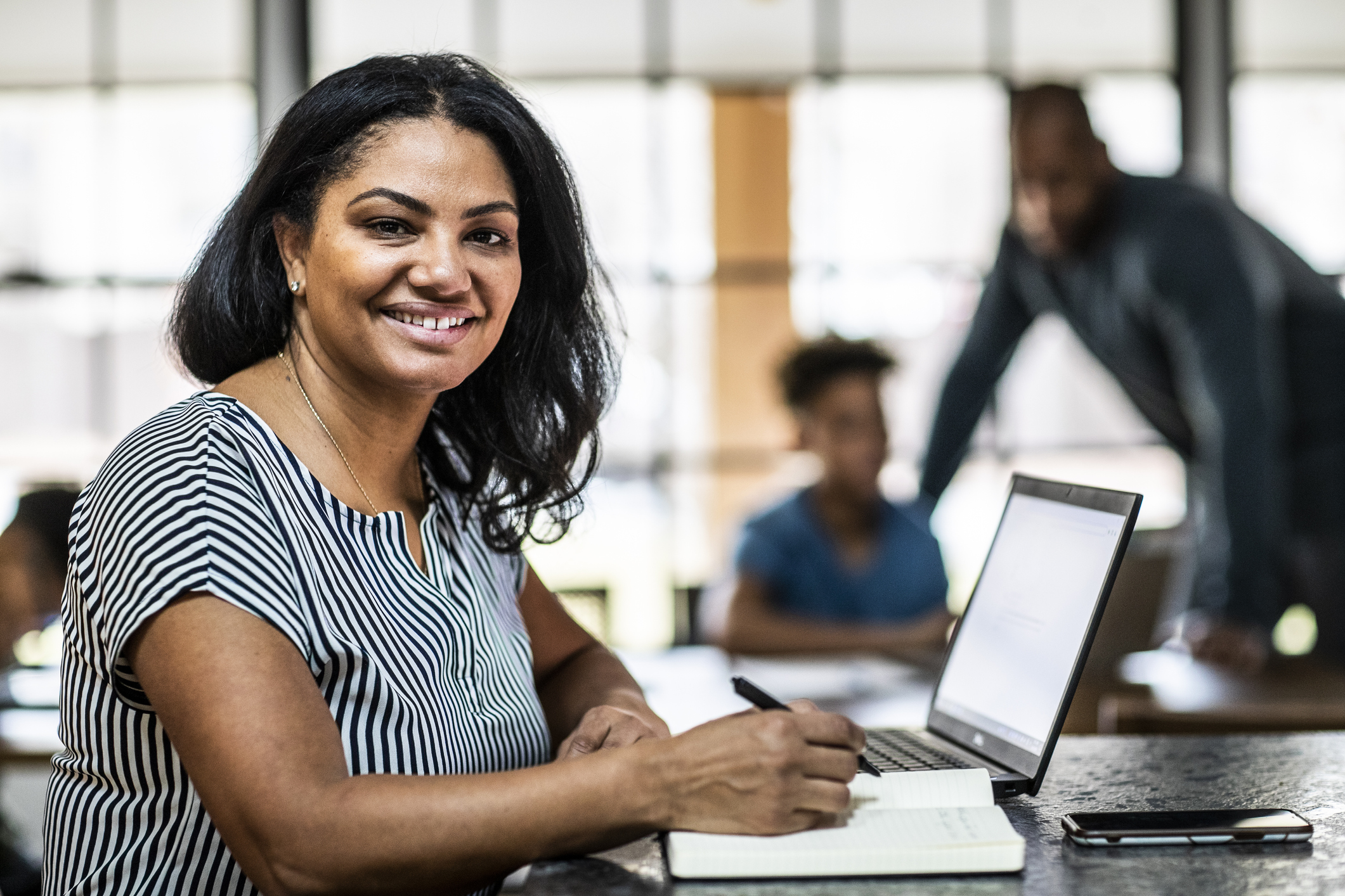 Portrait of mother working from home in residential kitchen with family in background